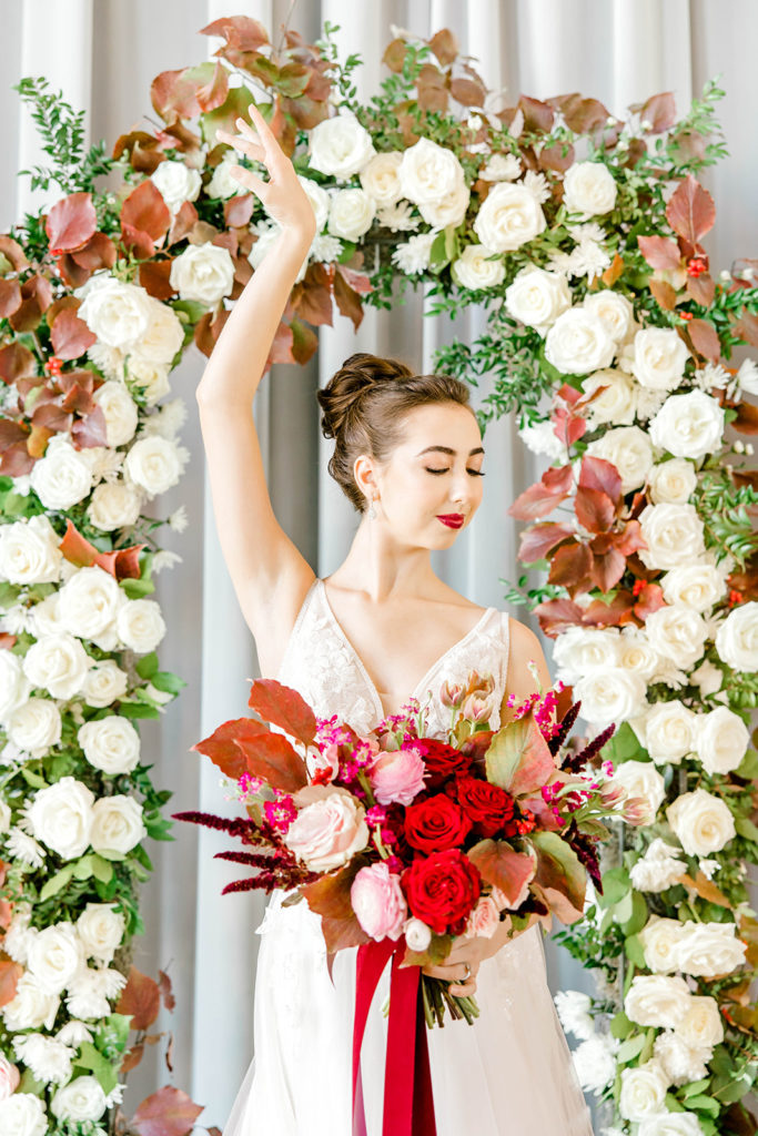 ballerina bride holding a bouquet and a ballet arm in front of floral arch